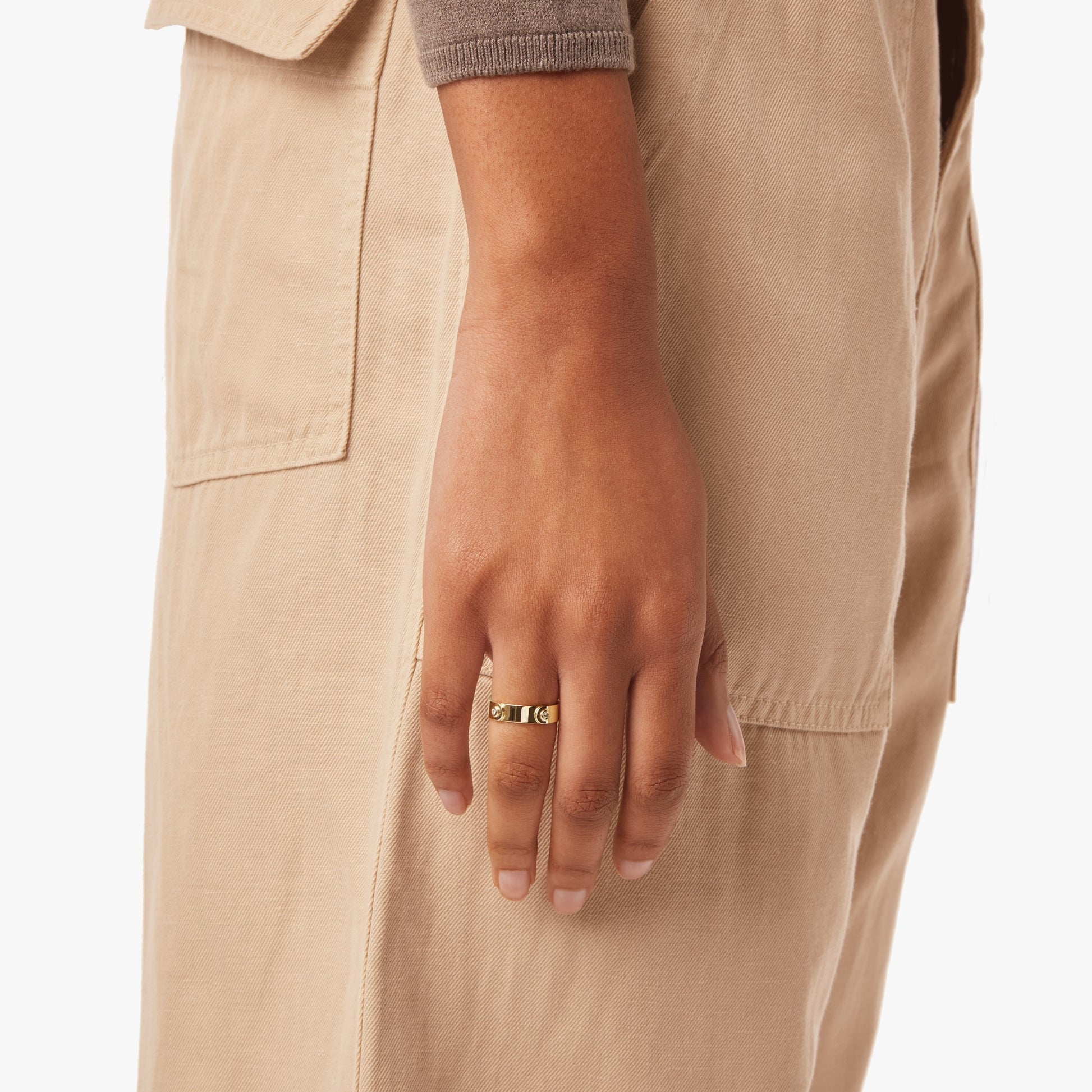 A person in a beige outfit with a long sleeve brown top, shown from the waist down. Their hand rests at their side against the fabric, showcasing the Shinola Diamond Rivet Plaque Ring in yellow gold.