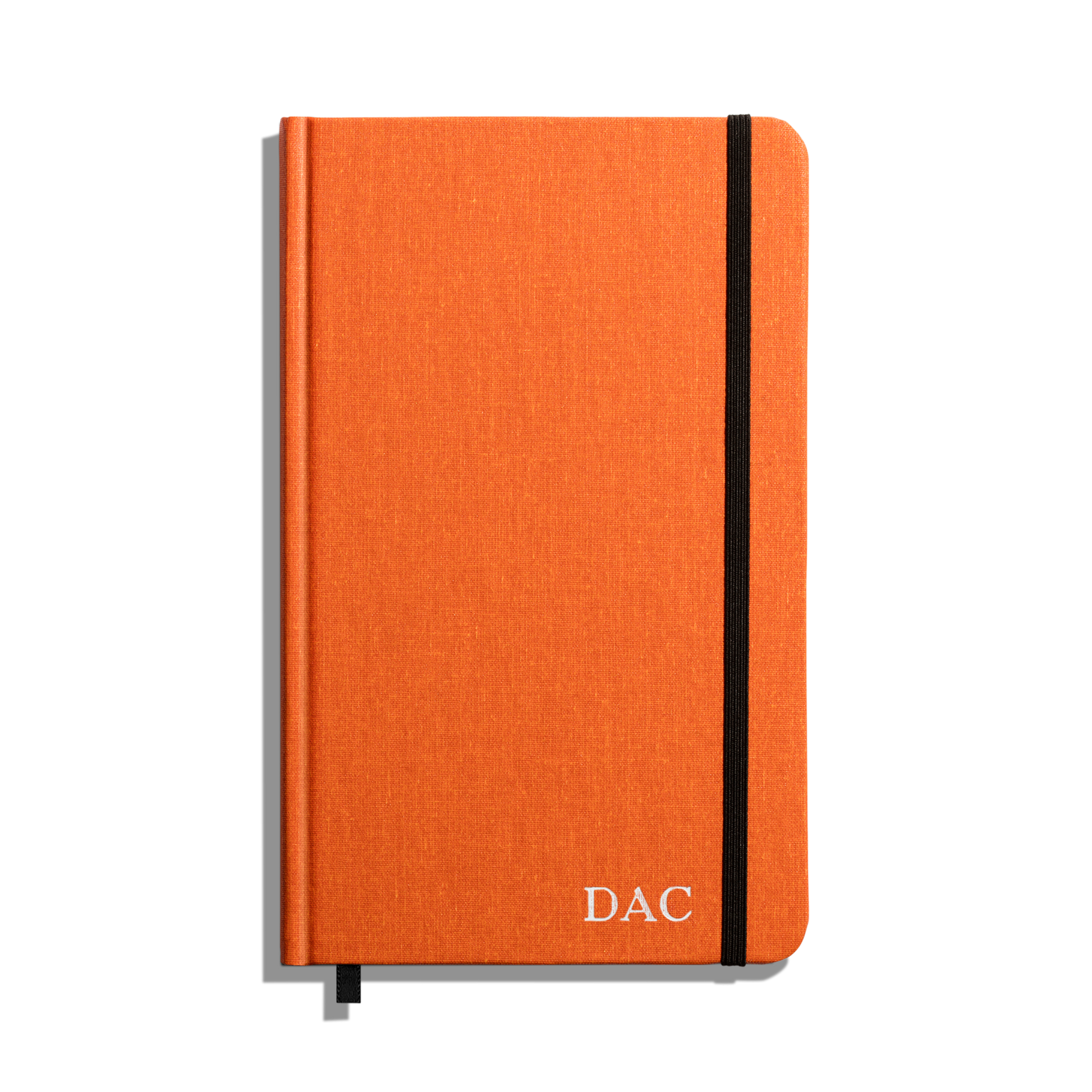 The Medium Hard Ruled Journal - Bold Orange by Shinola features a bold orange hardcover with “DAC” in white on the bottom right, a black elastic band, and ribbon bookmark. This American-made journal is set against a white background.