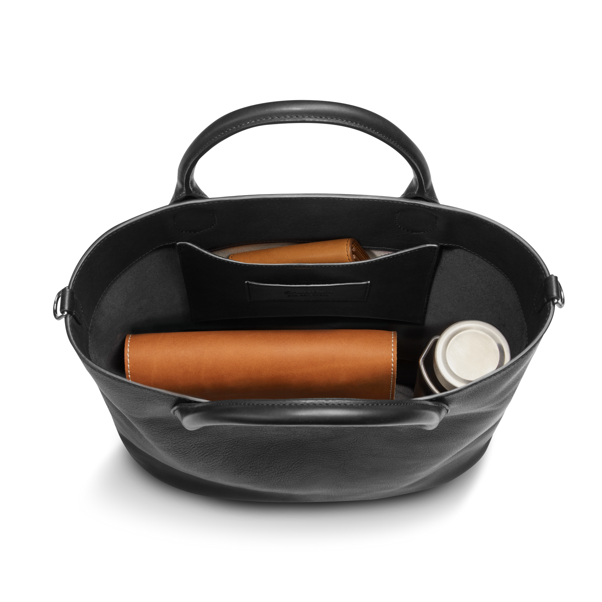 The Shinola 12 Hour Tote Bag - Black is shown from above, holding a brown wallet, brown glasses case, and silver water bottle. This everyday bag features short handles, an inner pocket, and neatly organizes your essentials.