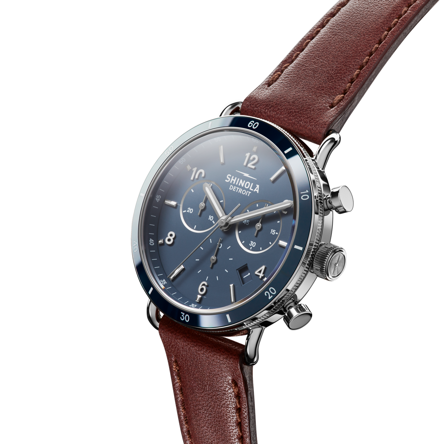A close-up of the Shinola Canfield Sport Chronograph Watch - Midnight Blue, featuring a blue dial, silver case, chronograph subdials, and a brown leather strap against a white background.