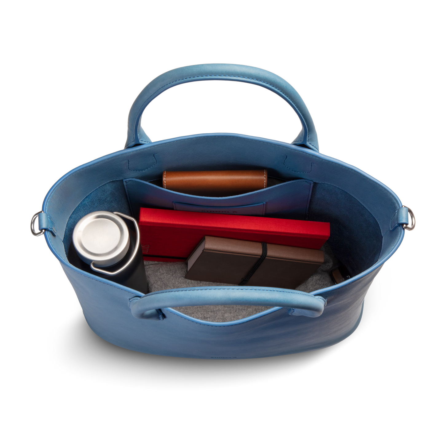 Top view of the Shinola 12 Hour Tote Bag - River in natural leather, open to show a stainless steel travel mug, a brown wallet, a red box, two smaller boxes, and a gray fabric item inside.