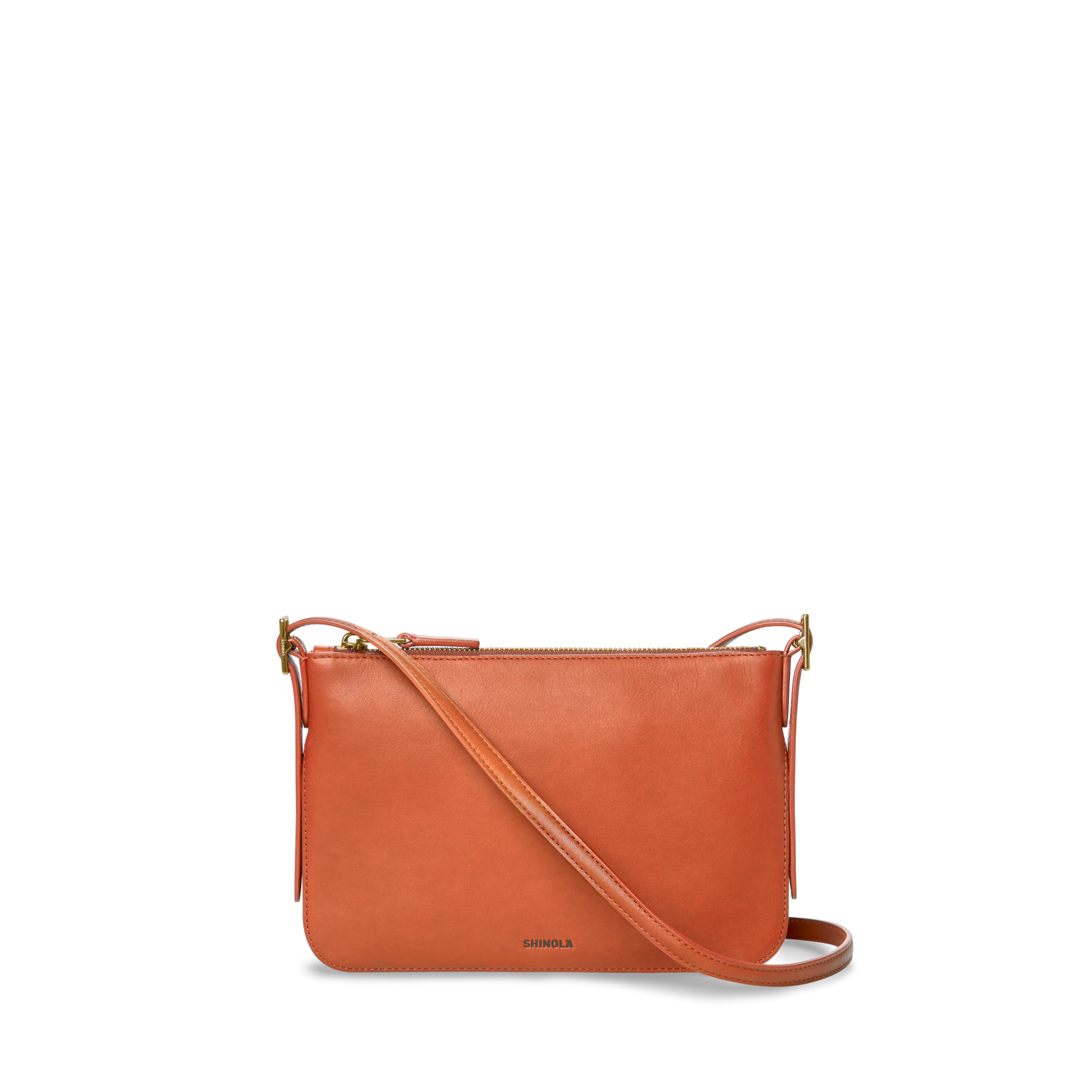 The Small Bixby Crossbody in Rust by Shinola is a small, rectangular bag crafted from natural leather with an adjustable strap and zippered top. The SHINOLA logo is printed near the bottom, making it a stylish everyday accessory.
