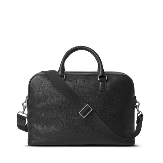 The Shinola Double Zip Briefcase - Black features natural grain leather, two top handles, a detachable shoulder strap, silver hardware, and an extra compartment, shown against a plain white background.
