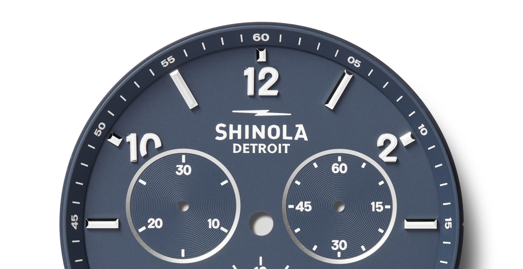 A close-up of the Shinola Canfield Sport Chronograph Watch in Midnight Blue features bold white hour markers, two subdials for seconds, and white minute markings along the edge. The watch hands are missing.