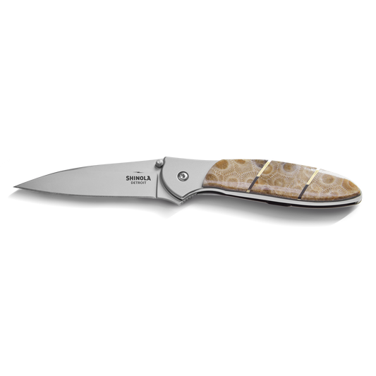 The Shinola + Kershaw Petoskey Stone Pocket Knife - Petoskey features a silver blade and a brown patterned handle with two thin gold bands, shown open against a white background.