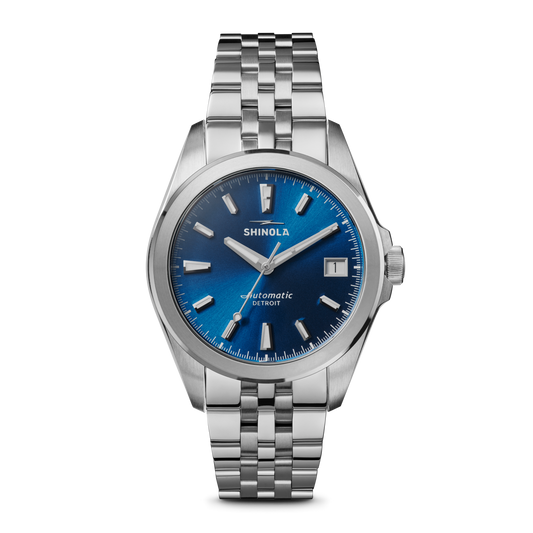 The Shinola Circadian Monster Automatic Watch - Daylight Blue features a stainless steel case, blue sunray dial, silver markers and hands, Swiss movement, date at 3 o'clock, and a metal link bracelet.