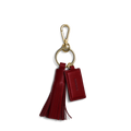 The Leather Tassel Keychain - Ruby by Shinola features a gold keyring with clasp, a red natural leather tassel, and a rectangular monogrammable tag embossed with SHINOLA. Shown on a plain white background.