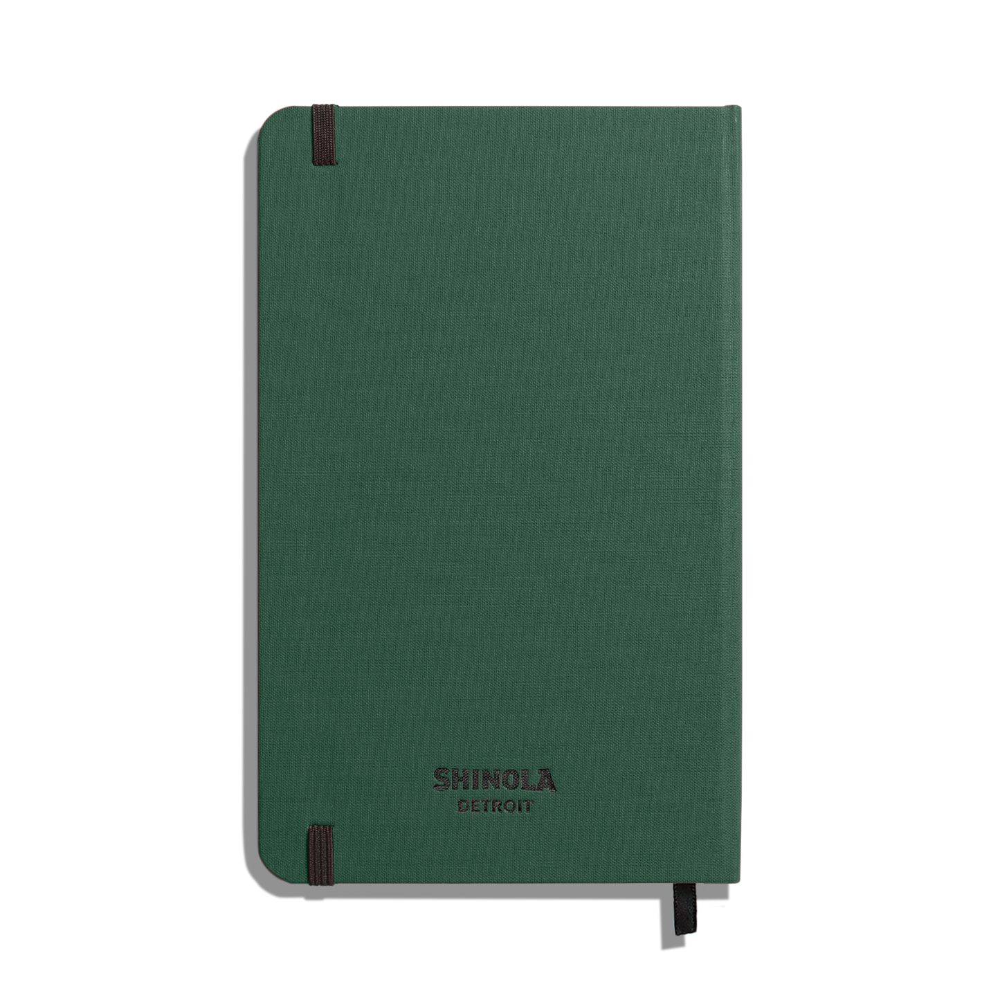A closed Shinola Medium Hard Ruled Journal - Forest sits against a white background, featuring a green textured cover, black elastic bands on two corners, and acid-free paper.
