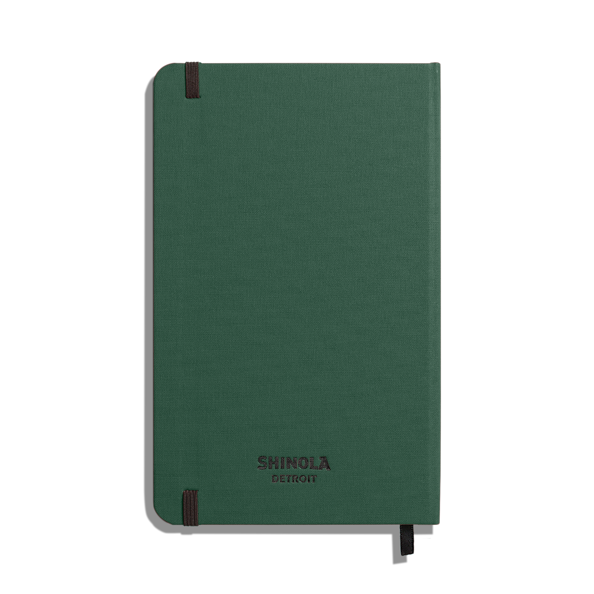 A closed Shinola Medium Hard Ruled Journal - Forest sits against a white background, featuring a green textured cover, black elastic bands on two corners, and acid-free paper.
