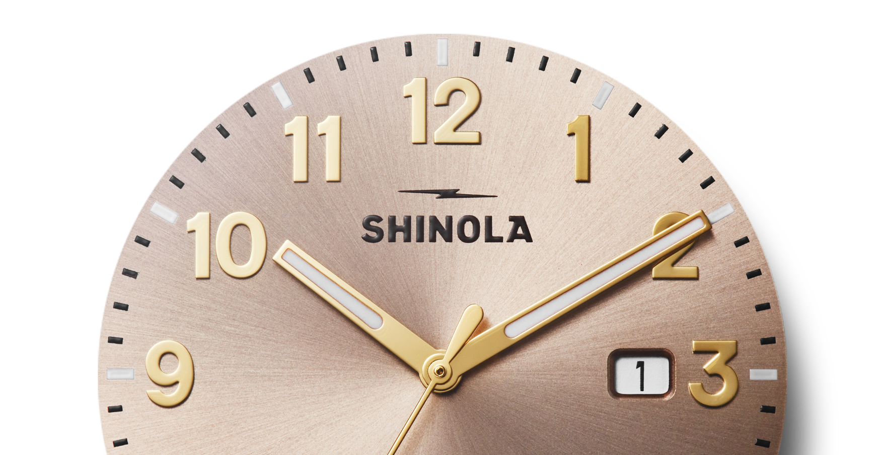 Close-up of the Shinola Detrola Watch - Nude, featuring gold numbers and hands, a small date window near 3, and a brushed metallic face—highlighting classic American design. Time displayed is about 10:10.
