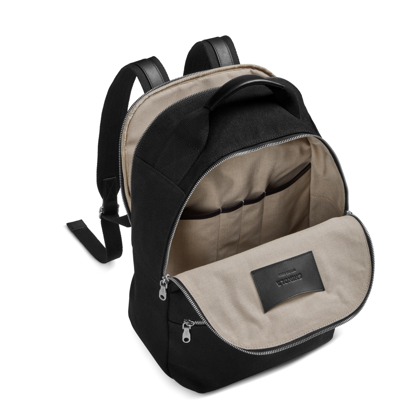 The Shinola Runwell Canvas Backpack - Black features a beige interior with multiple inner pockets, two zippers, adjustable shoulder straps, and a black label on the inner flap—a durable choice for everyday use.