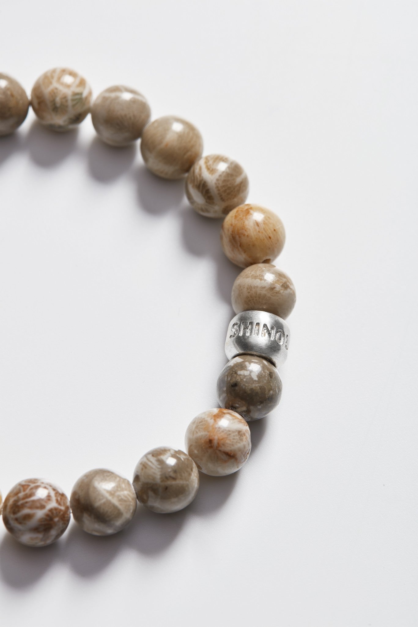 Close-up of Shinola’s 8mm Beaded Petoskey Bracelet featuring polished brown and beige Petoskey stones and a sterling silver JOURNEY bead, shown on a white background—a distinctive Michigan jewelry piece.