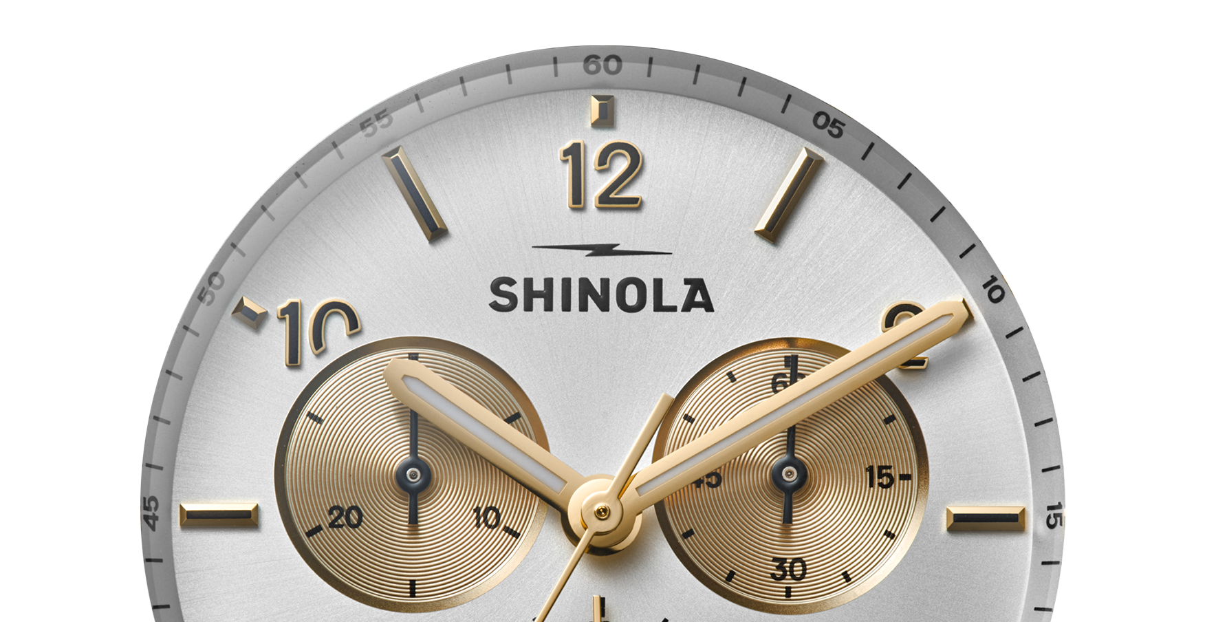 Close-up of the Shinola Canfield Sport Chronograph Watch - Silver, featuring gold hour markers and hands, subdials at 3 and 9 o’clock, a silver face, and the Shinola logo at center.