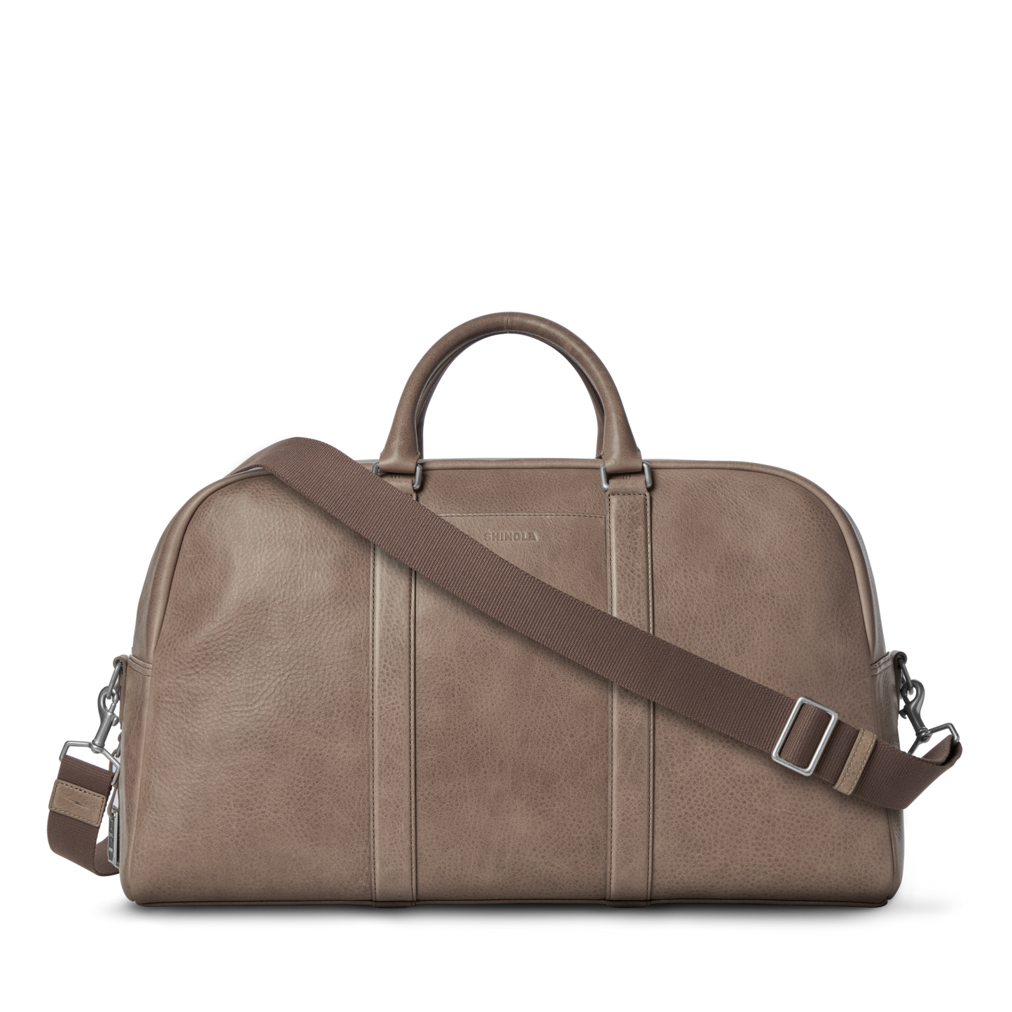 The Shinola Runwell Duffle Bag - Stone features natural grain leather in taupe, two handles, an adjustable brown shoulder strap, silver hardware, and a subtle embossed logo. This minimalist carry-on offers modern style.