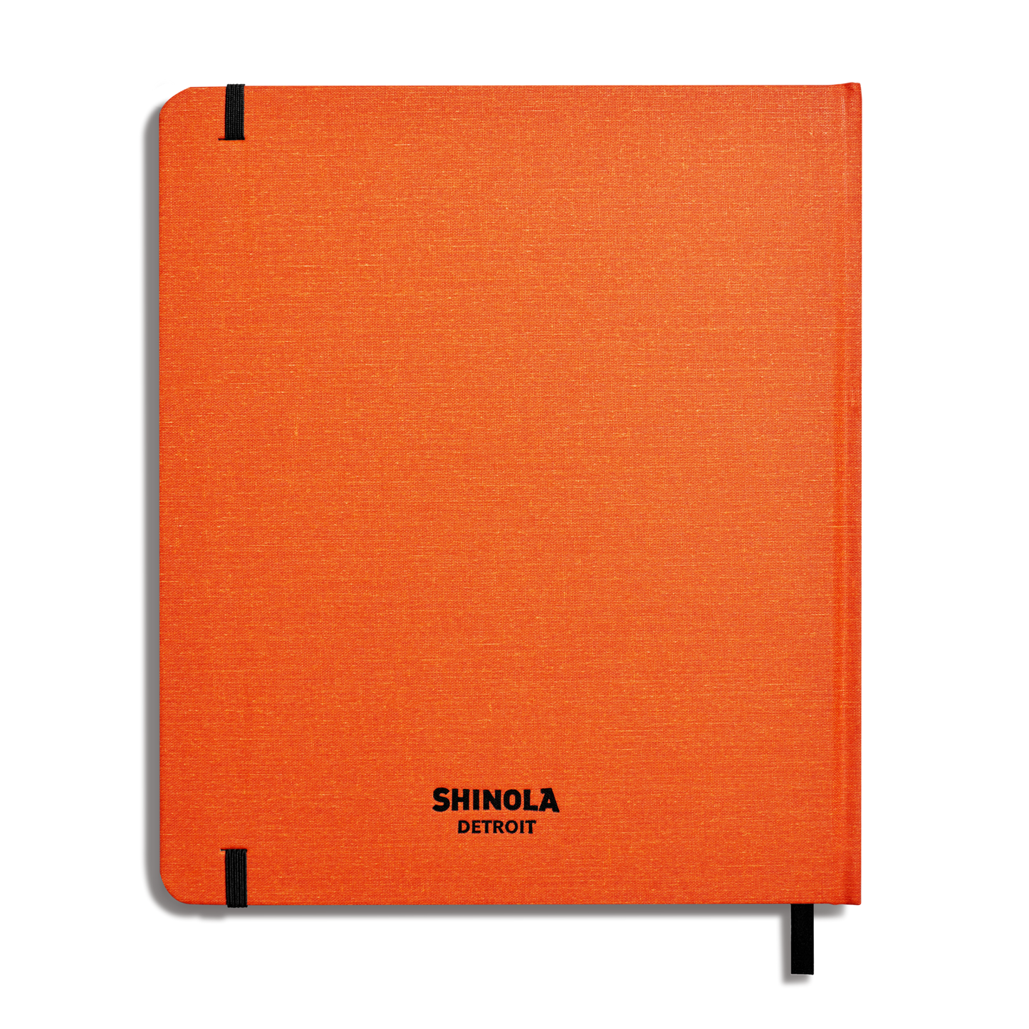 The Shinola Large Hard Plain Sketchbook in bold orange features black corner elastics, a black ribbon bookmark, and “SHINOLA DETROIT” printed in black at the lower center of its American-made hardcover.