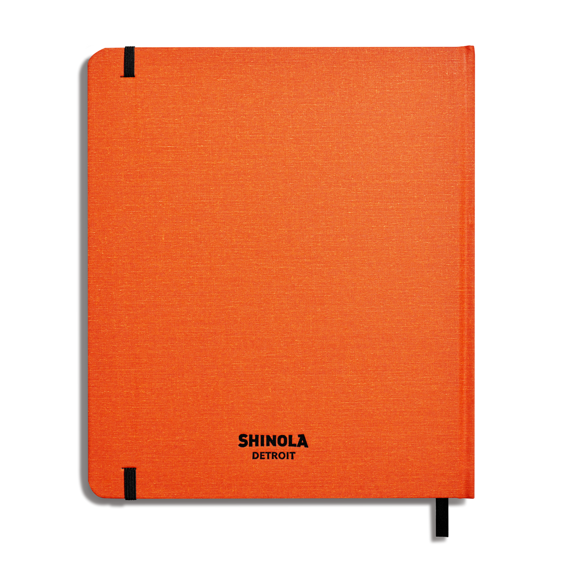 The Shinola Large Hard Plain Sketchbook in bold orange features black corner elastics, a black ribbon bookmark, and “SHINOLA DETROIT” printed in black at the lower center of its American-made hardcover.