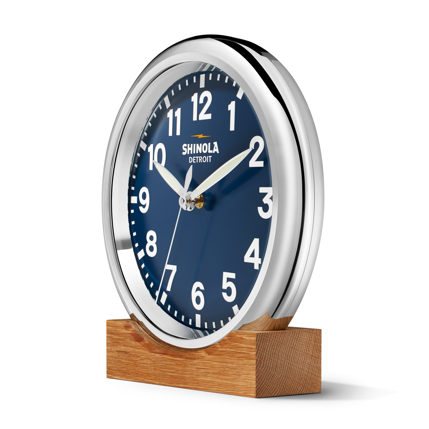 A 14" Shinola Runwell Clock - Navy with a matte midnight blue dial, white numbers and shiny silver frame sits on a rectangular wooden base. The face reads 10:10 and displays "Shinola Detroit.