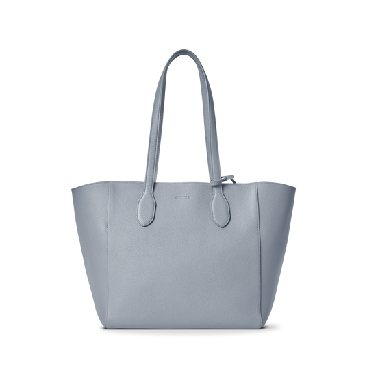 The Shinola Runabout Tote Bag - Mist features light blue pebbled leather, two shoulder straps, a structured design, subtle stitching, and an interior zipper pouch, shown against a plain white background.