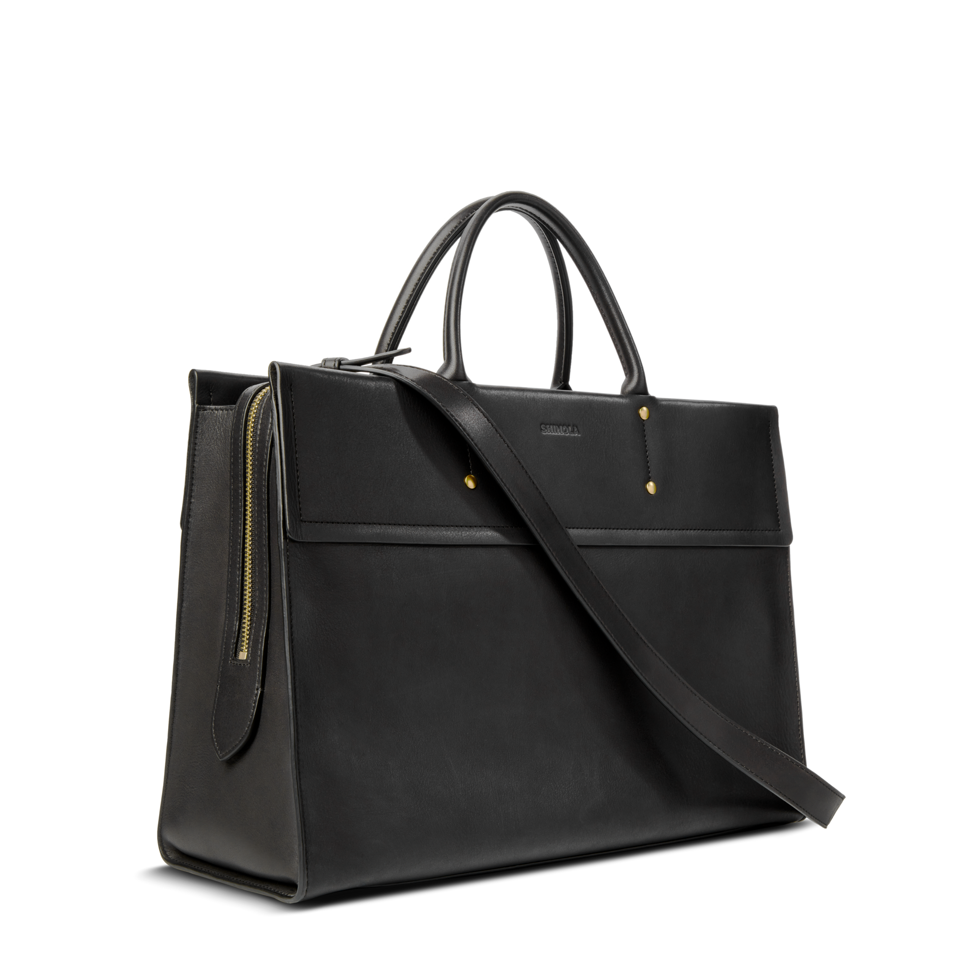 The Shinola Day Satchel - Black features two top handles, a long shoulder strap, gold-tone studs, and a side zipper detail. This versatile leather bag is perfect for on-the-go use and is photographed against a plain white background.