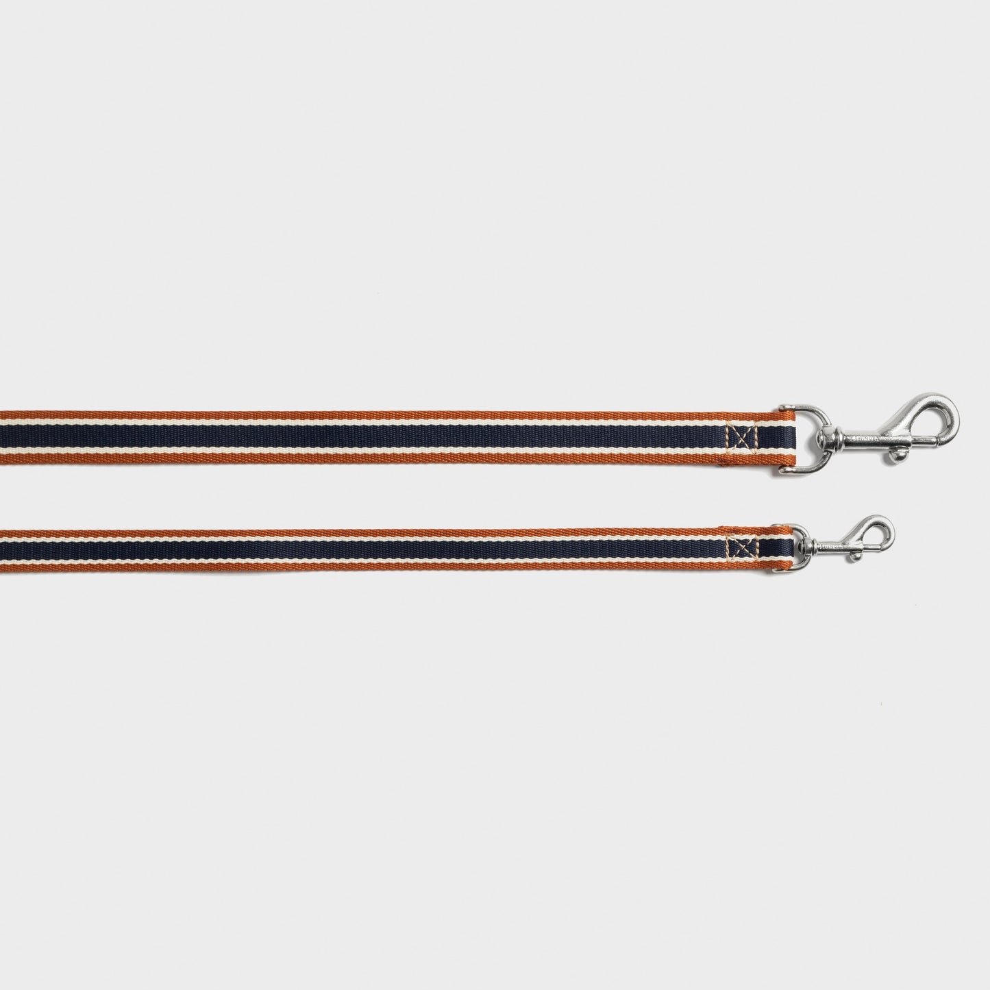 Two Shinola Nylon Dog Leash - Brand Stripe leashes in orange, black, and white with silver clasps are laid flat on a white background. Durable and stylish, they combine Shinola's signature strength with vibrant design.