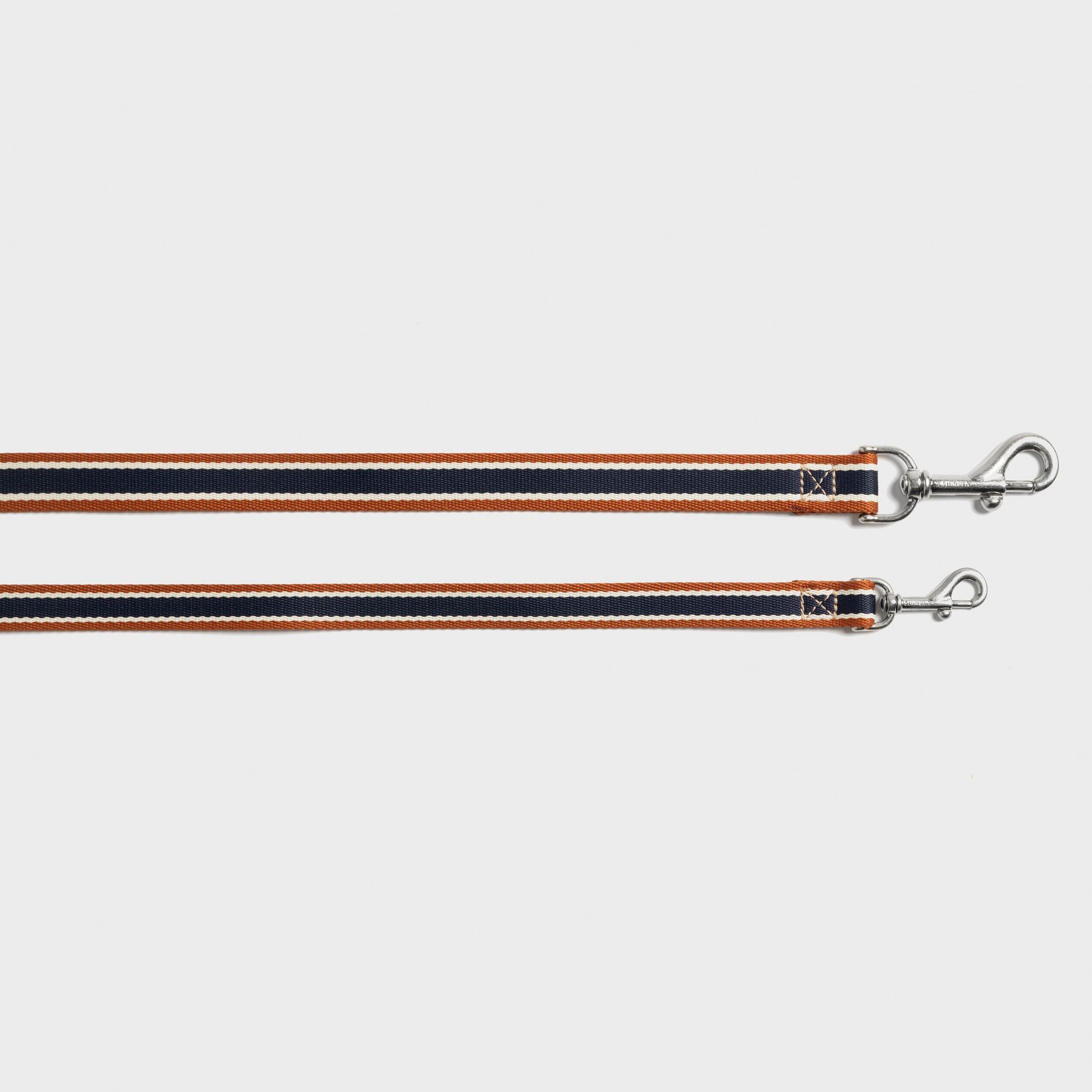 Two Shinola Nylon Dog Leash - Brand Stripe leashes in orange, black, and white with silver clasps are laid flat on a white background. Durable and stylish, they combine Shinola's signature strength with vibrant design.