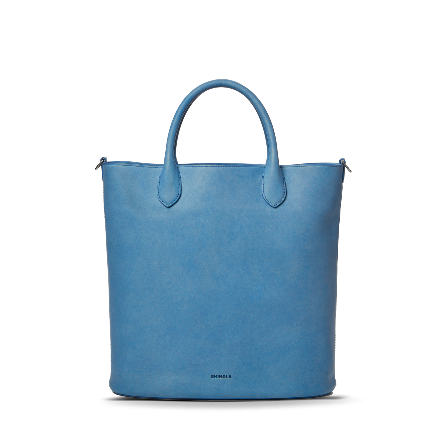 The Shinola 12 Hour Tote Bag - River is a structured, light blue tote crafted from natural leather with two rounded handles and a subtle Shinola logo at the bottom center, shown on a plain white background.