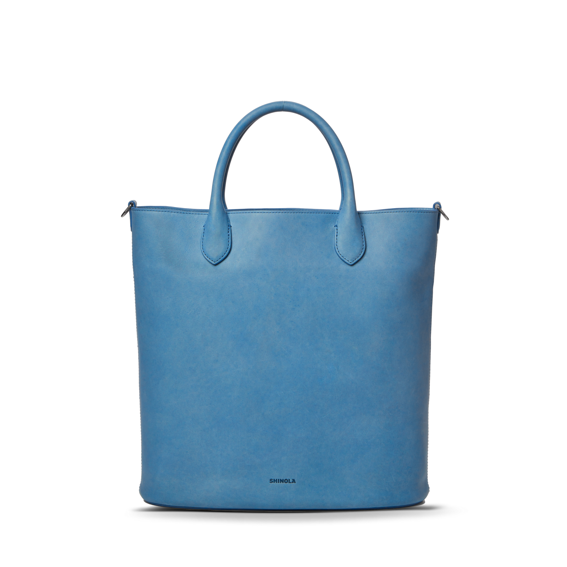 The Shinola 12 Hour Tote Bag - River is a structured, light blue tote crafted from natural leather with two rounded handles and a subtle Shinola logo at the bottom center, shown on a plain white background.