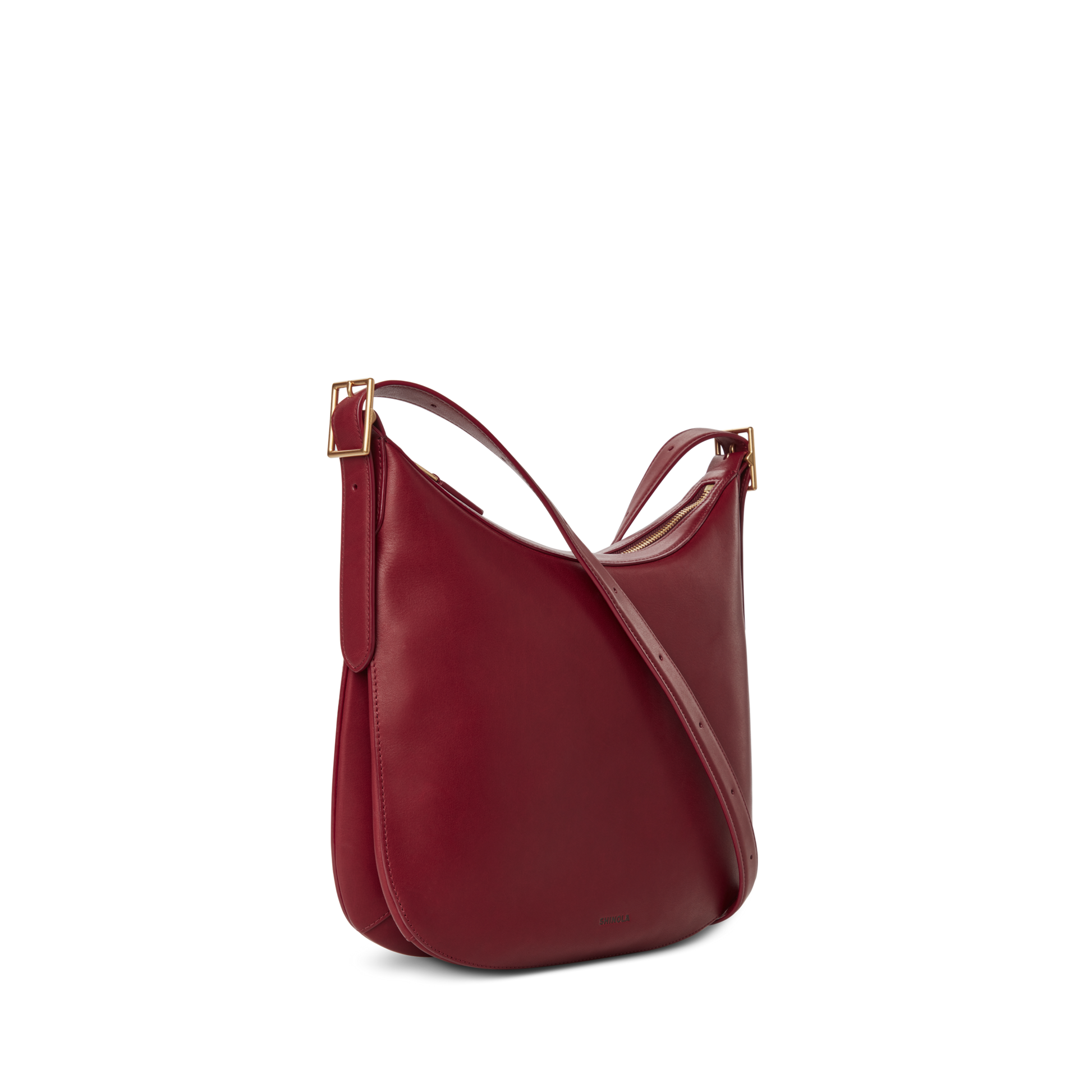 The Shinola Medium Bixby Crossbody - Ruby features a curved silhouette, adjustable strap, and gold-tone buckle accents, shown against a plain white background for an effortlessly versatile look.
