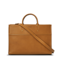The Day Satchel - Tan by Shinola features tan leather, short round handles, a long adjustable shoulder strap, a front pocket, gold hardware accents, and an embossed brand logo—its structured rectangular shape makes it ideal for on-the-go use.