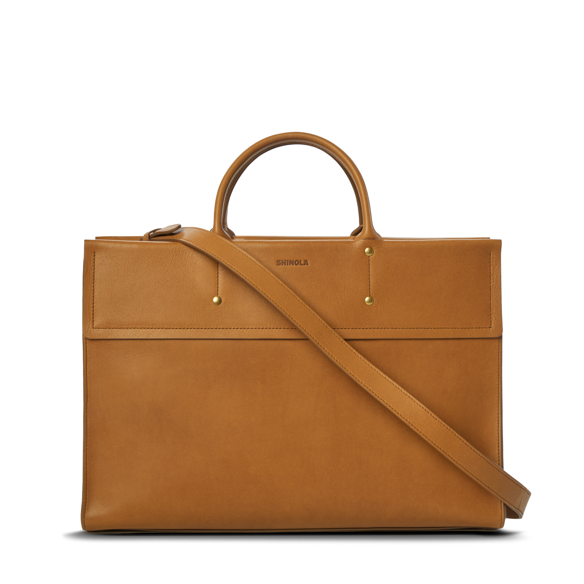 The Day Satchel - Tan by Shinola features tan leather, short round handles, a long adjustable shoulder strap, a front pocket, gold hardware accents, and an embossed brand logo—its structured rectangular shape makes it ideal for on-the-go use.