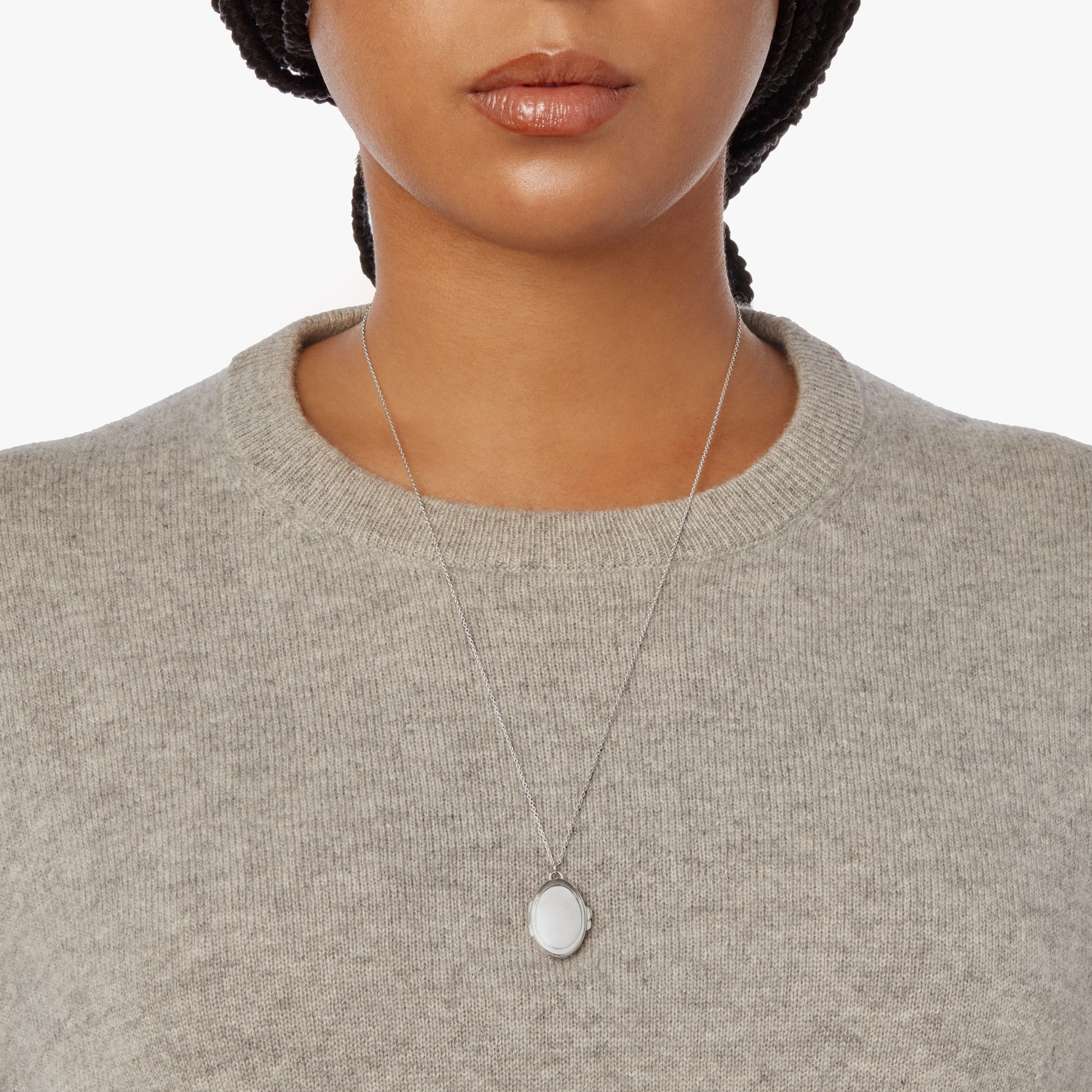 A woman wears the Shinola Heirloom Statement Locket Necklace in sterling silver and a light gray knit sweater, shown from the shoulders up against a plain white background.