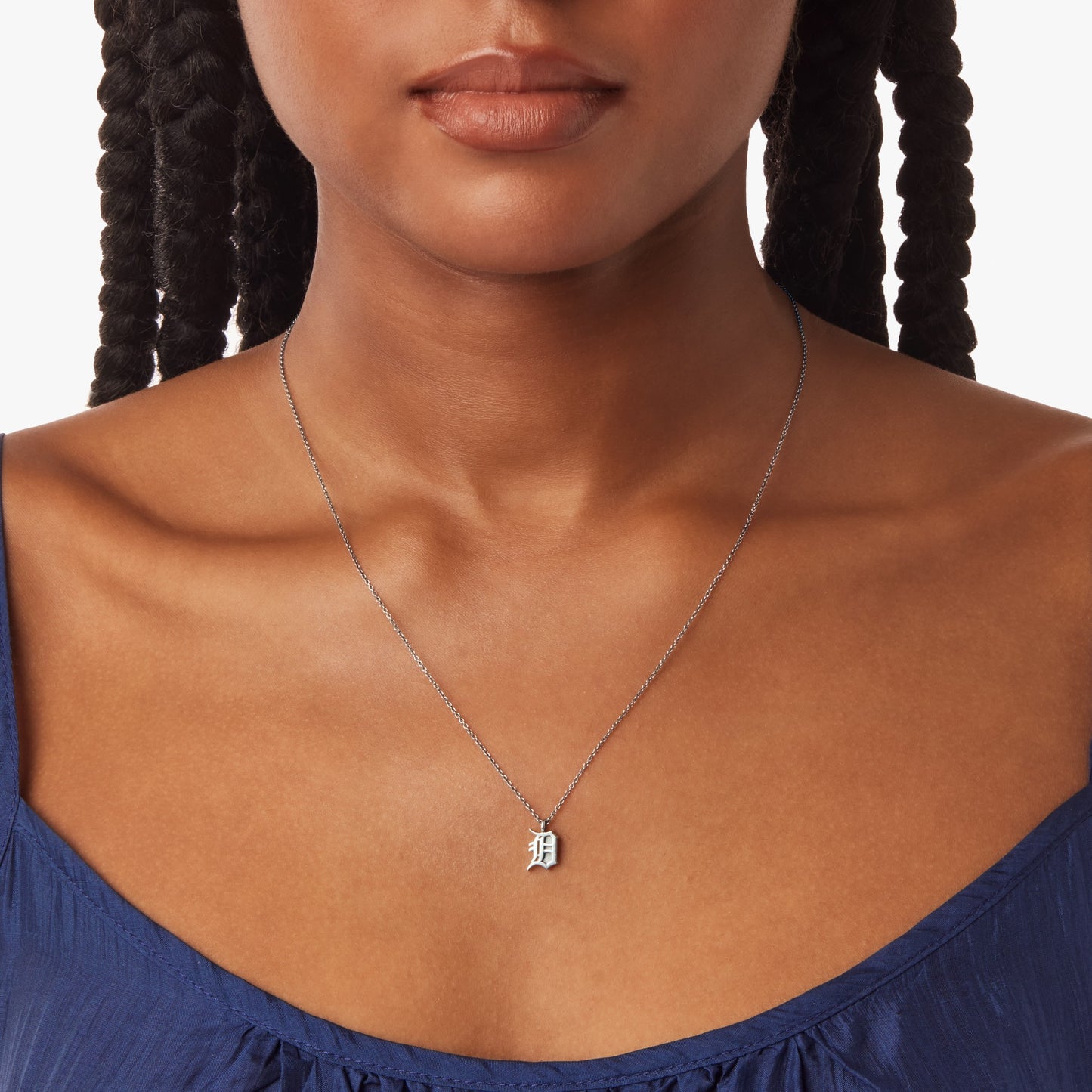 A woman wears a blue top and the Shinola Detroit "D" Charm Necklace in sterling silver. The image, cropped from the shoulders up, spotlights this distinctive piece of Detroit-inspired jewelry.