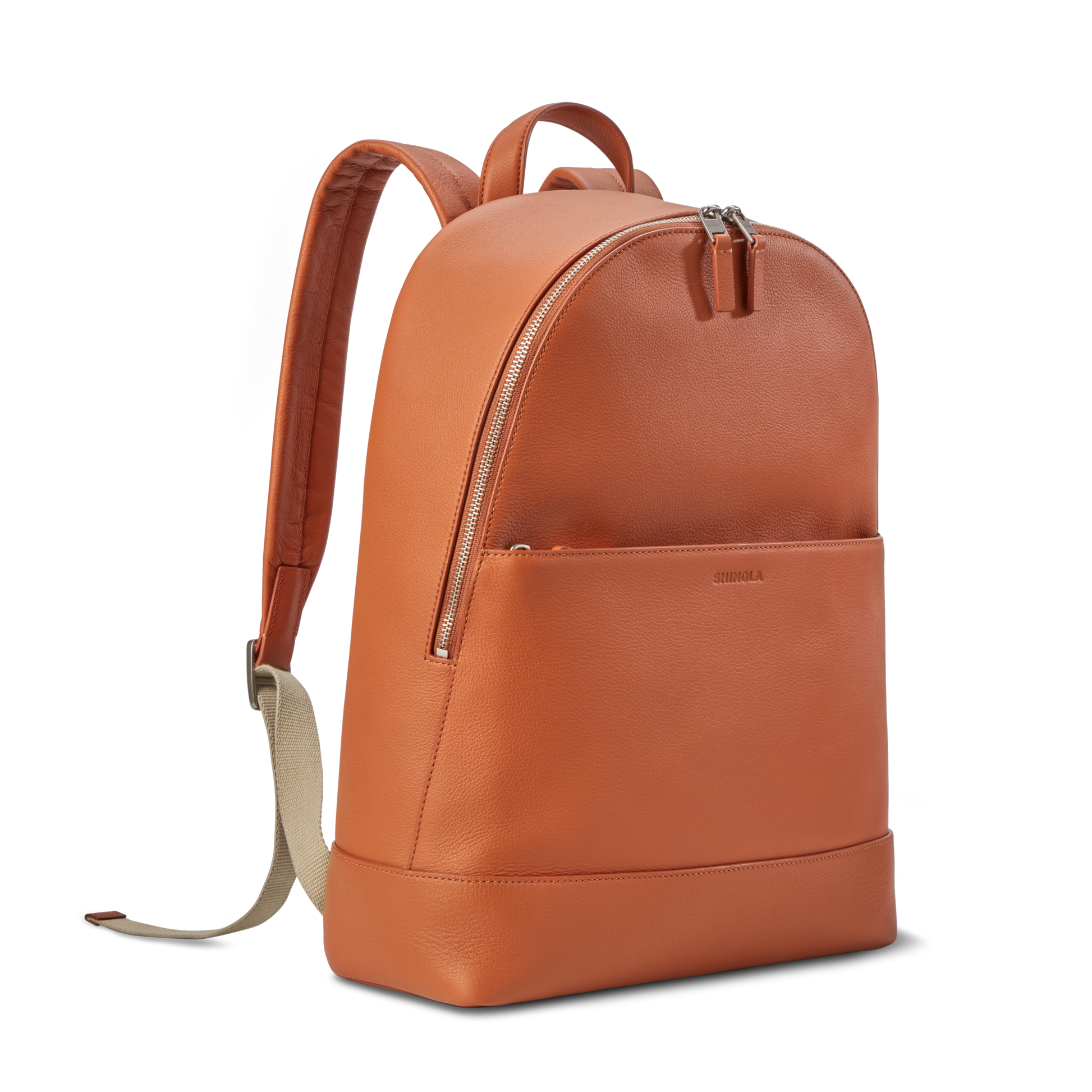 The Shinola Canfield Backpack in Rust features orange leather, a front zip pocket, beige adjustable straps, and a top handle—ideal as a laptop backpack for work or travel—shown on a plain white background.