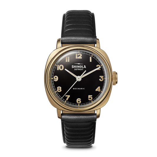 The Shinola Mechanic Watch - Black/Gold features a gold case, black dial, black leather strap, and an exhibition case back.