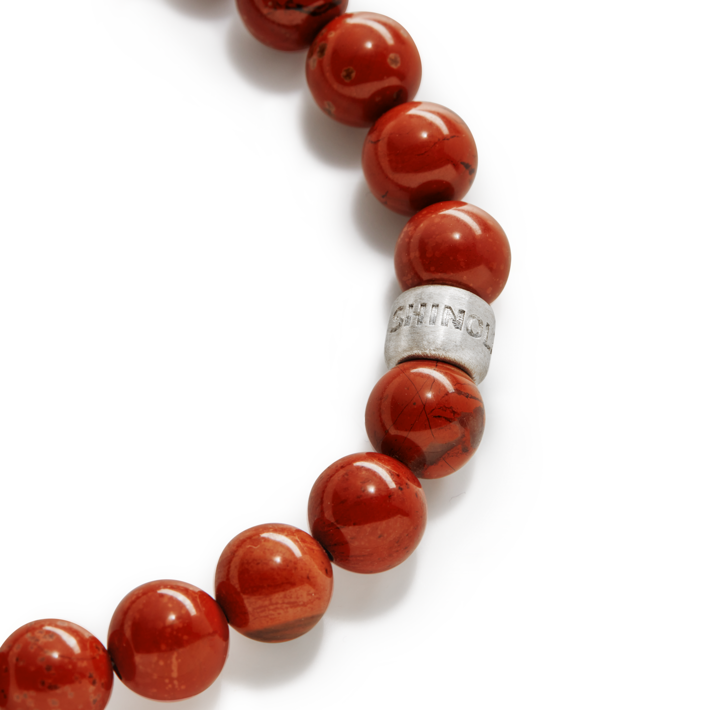 A close-up of Shinola's 8mm Beaded Red Jasper Bracelet, showcasing polished red jasper beads and a sterling silver accent engraved with SHINOLA.