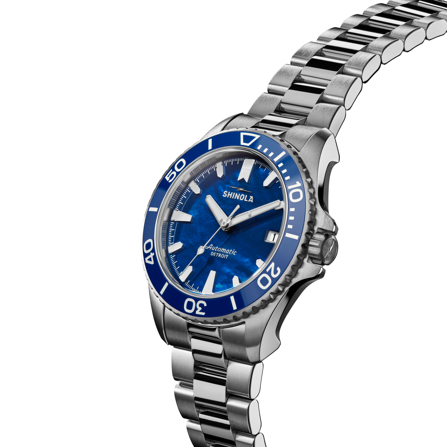 The Shinola Lake Michigan Monster Automatic Dive Watch features a blue dial and bezel, silver hour markers, a stainless steel link bracelet, and "Automatic" and "Shinola" on the white-background dial.