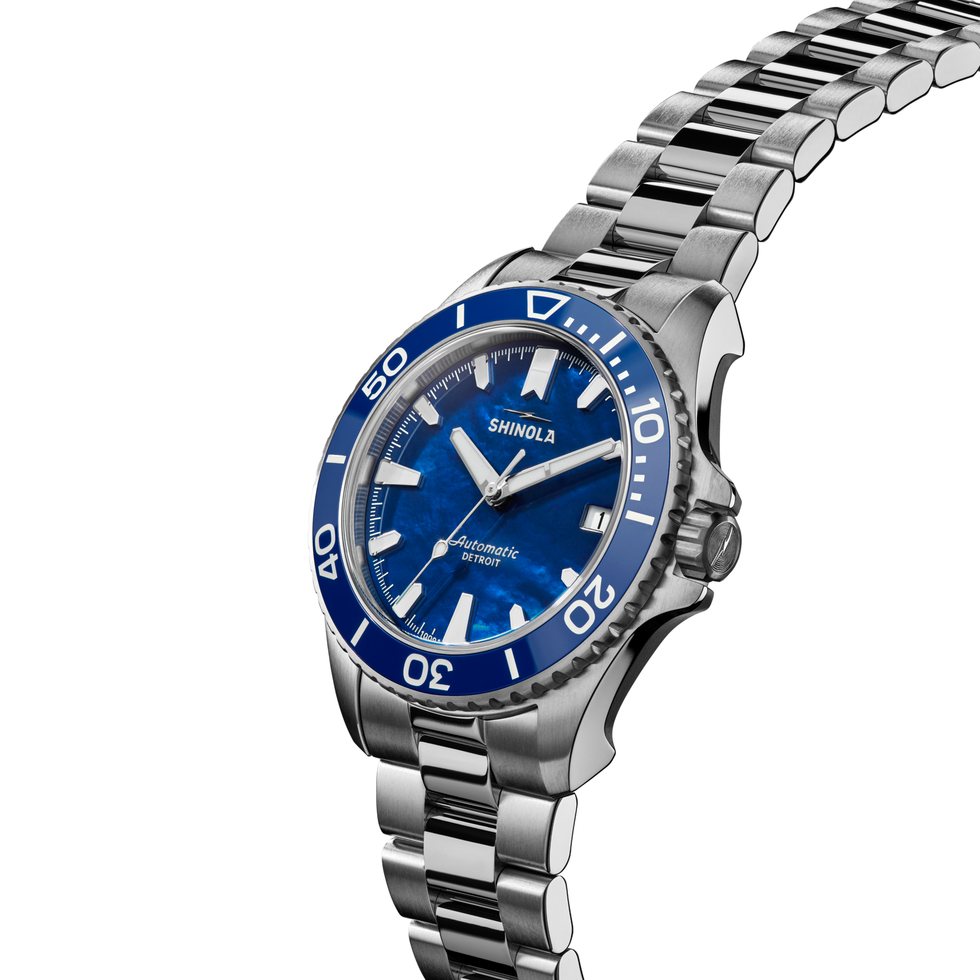 The Shinola Lake Michigan Monster Automatic Dive Watch features a blue dial and bezel, silver hour markers, a stainless steel link bracelet, and "Automatic" and "Shinola" on the white-background dial.