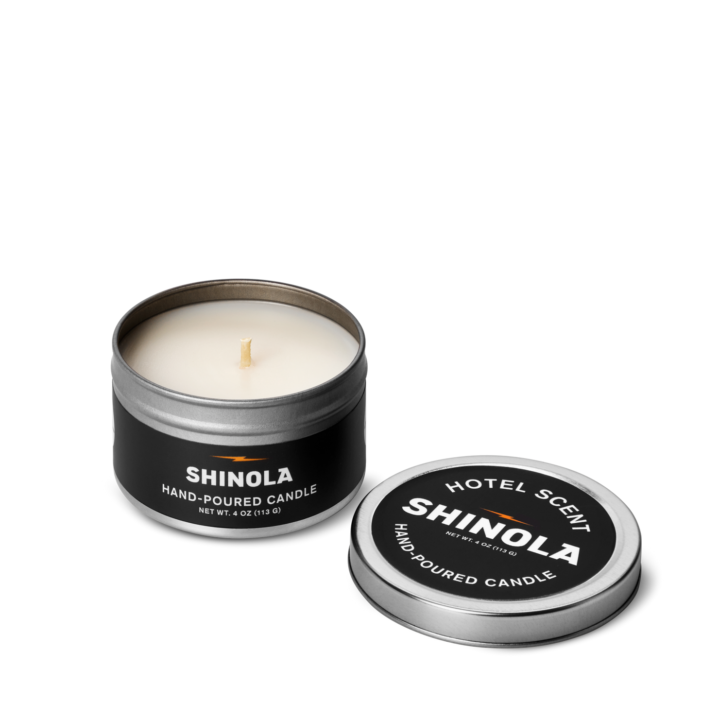 A white Shinola Hand Poured 4oz Travel Candle – Hotel sits in a small tin with its black lid, which reads “Shinola Hotel Scent Hand-Poured Candle,” placed beside it. The portable candle is made from coconut soy wax.