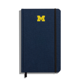 The Shinola Medium Hard Ruled Journal in navy features a yellow University of Michigan M logo on the cover, a black elastic band closure on the right side, and a black ribbon bookmark at the bottom.