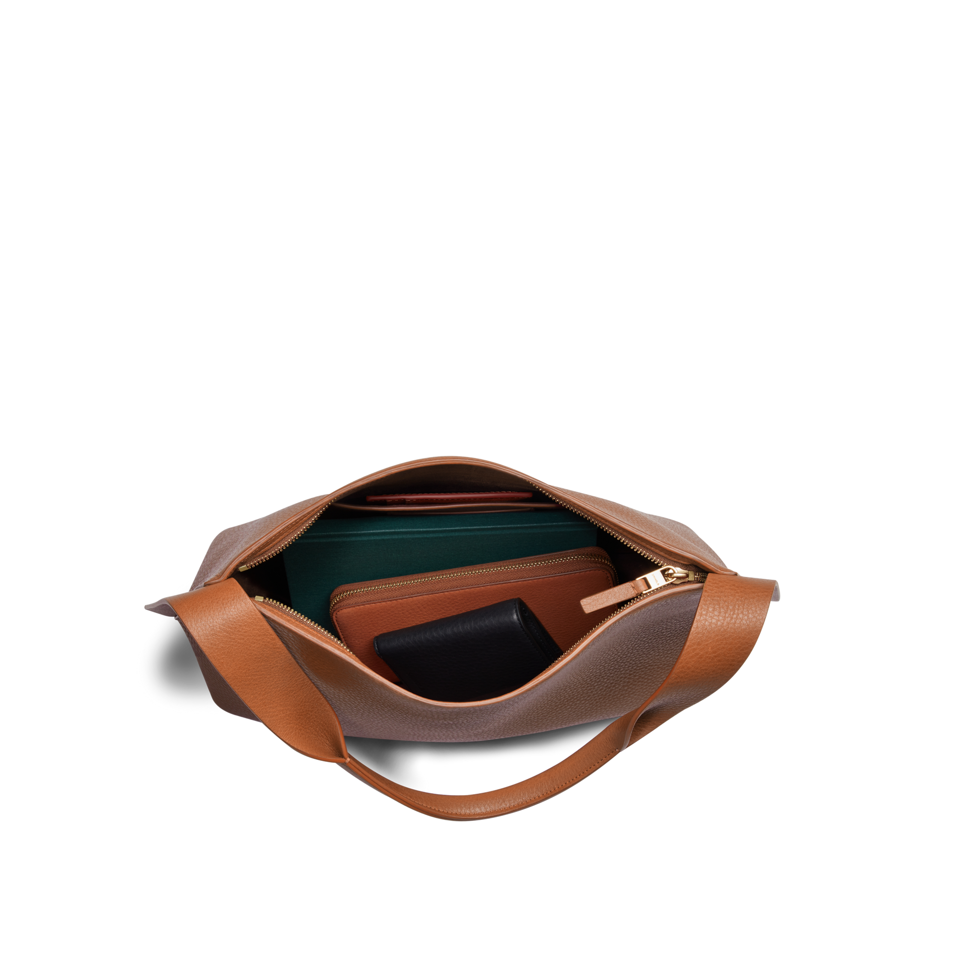 Top view of an open Shinola Medium Derby Shoulder Bag - Tan with a zipper, showing a green notebook, brown wallet, and black pouch inside on a plain white background.