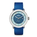 The Shinola Detrola Watch - Blue features a round face with a silver bezel, blue dial, minimalist markers, date at 3 o’clock, and a blue leather strap—a contemporary accessory for modern style.