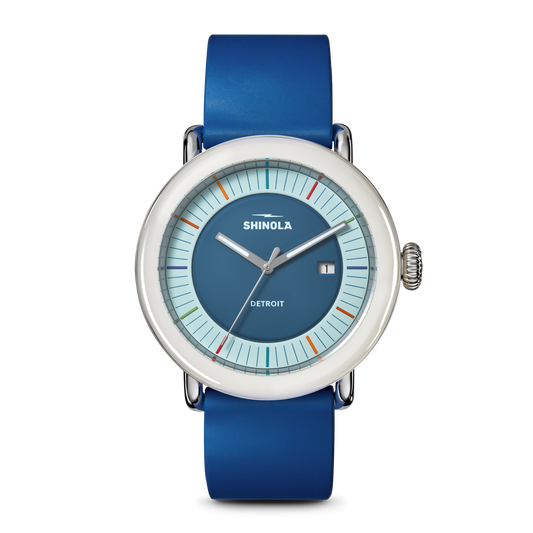 The Shinola Detrola Watch - Blue features a round face with a silver bezel, blue dial, minimalist markers, date at 3 o’clock, and a blue leather strap—a contemporary accessory for modern style.