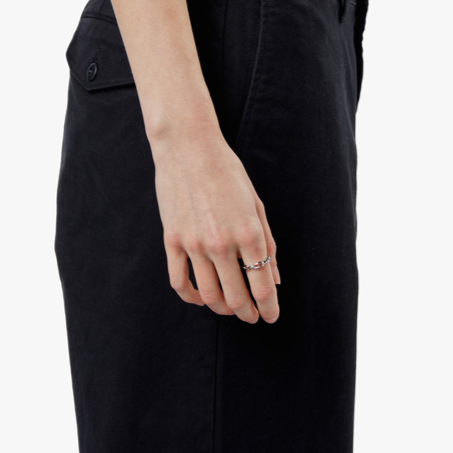 A person in black pants is shown from the waist down, their left hand by their side, wearing the Shinola Signature Link Ring in sterling silver. The silver ring features small round details. The background is white.
