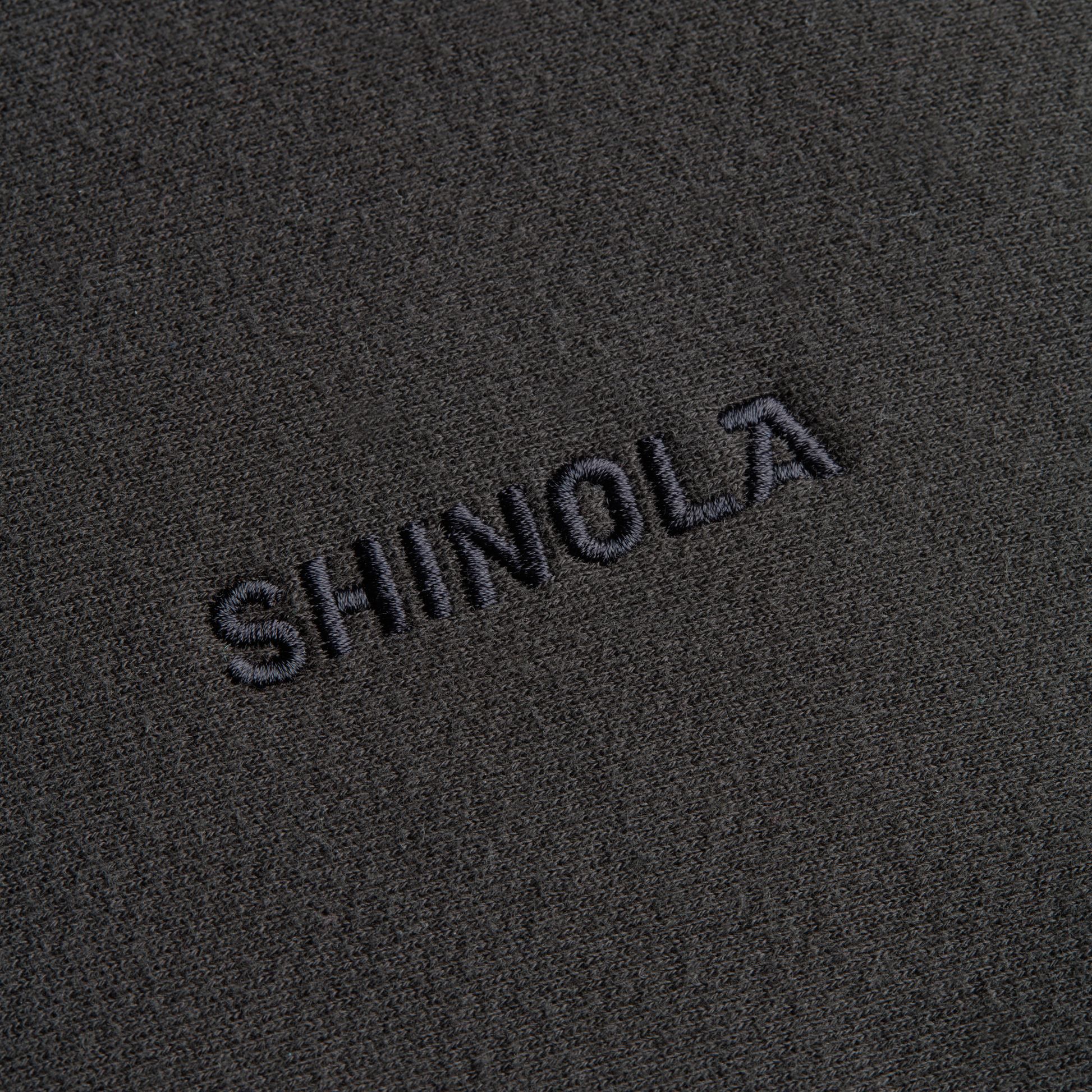 Close-up of the Shinola Fleece Logo Sweatshirt - Vintage Black, showing dark gray textured fabric and "SHINOLA" embroidered in bold black letters. Made from unisex classic fit American cotton fleece.
