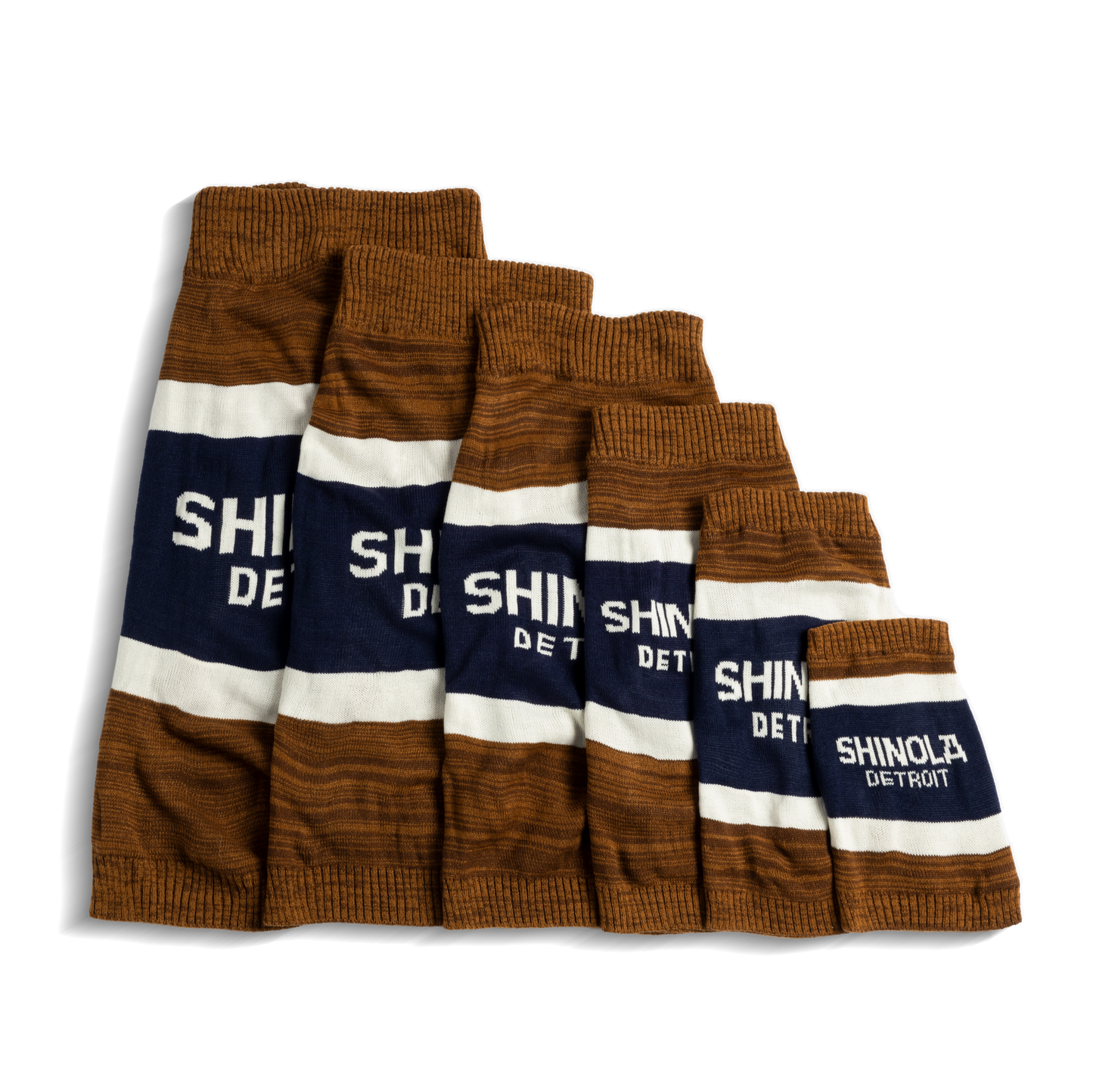 Six tan Shinola dog sweaters with brand stripes, arranged in descending size order from left to right—each featuring the Shinola logo—perfect for pairing with your favorite Shinola gear.
