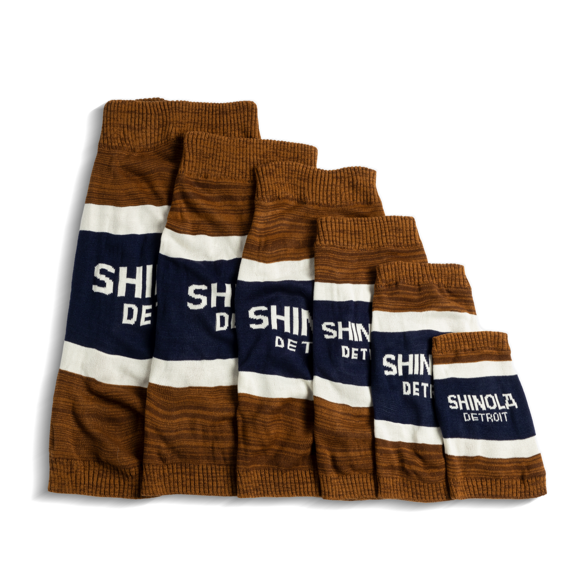 Six tan Shinola dog sweaters with brand stripes, arranged in descending size order from left to right—each featuring the Shinola logo—perfect for pairing with your favorite Shinola gear.