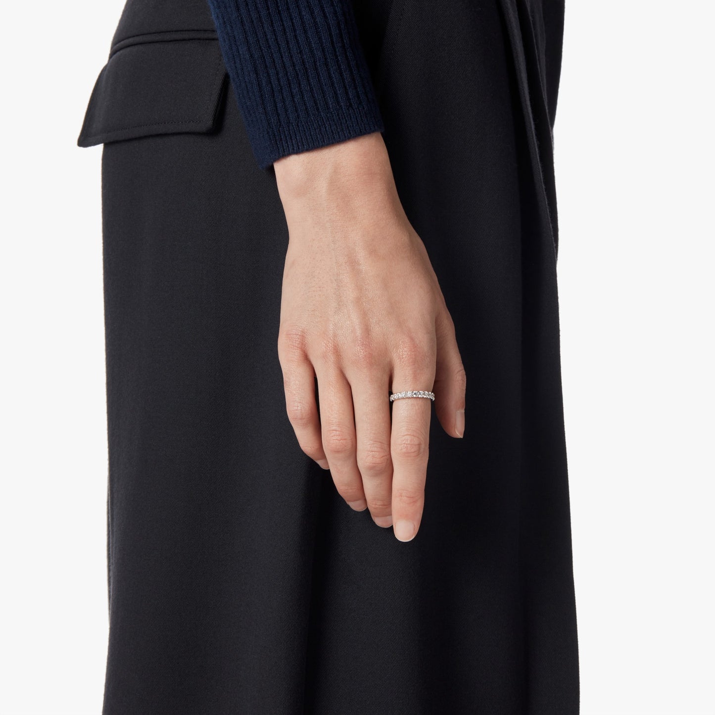 A close-up of a person’s hand wearing the Shinola 1 Carat Diamond Anniversary Band in white gold on their ring finger, with their arm at their side. They are dressed in a dark, long-sleeved top and skirt.