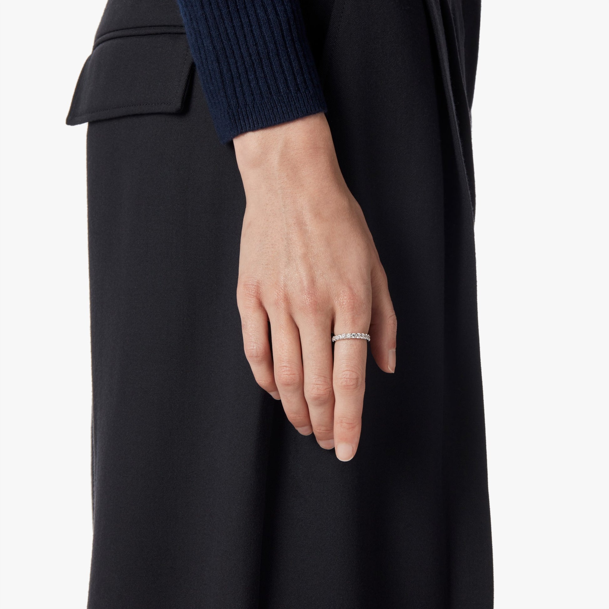 A close-up of a person’s hand wearing the Shinola 1 Carat Diamond Anniversary Band in white gold on their ring finger, with their arm at their side. They are dressed in a dark, long-sleeved top and skirt.