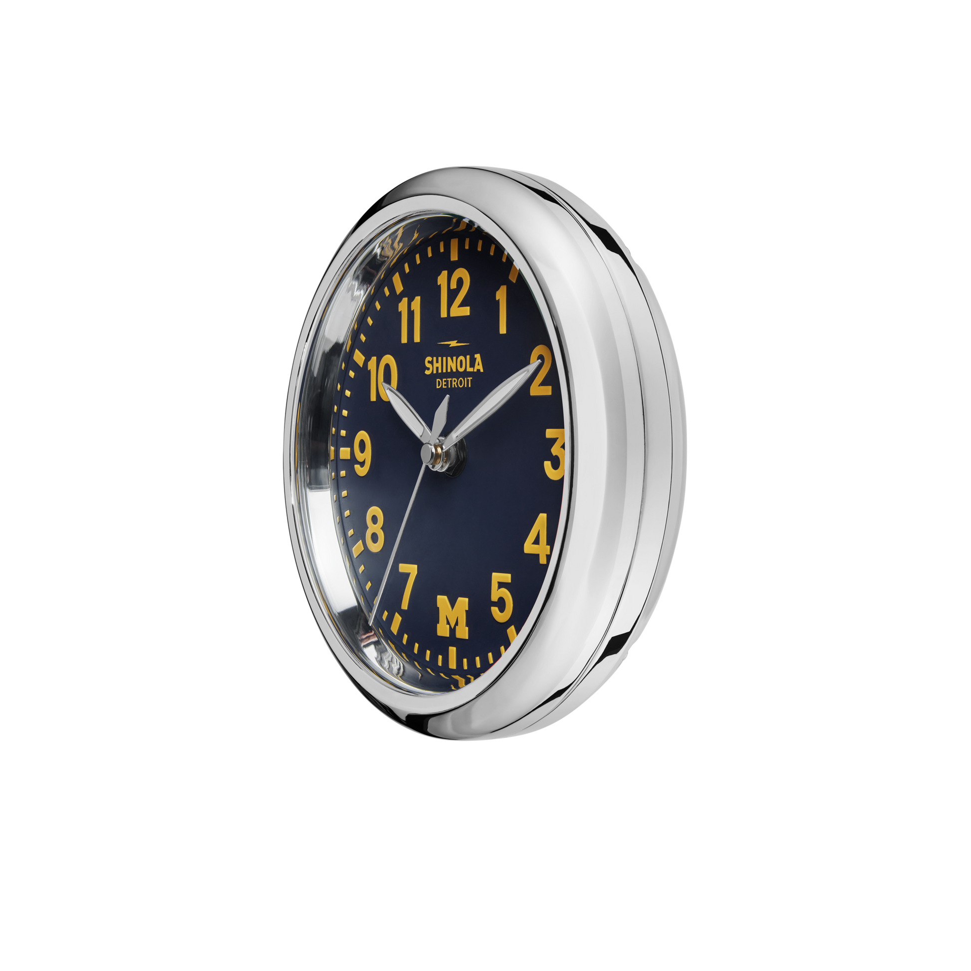 The 6" Runwell Clock - Blue by Shinola features a round chrome frame, wolverine blue face, yellow numerals and hands, plus the Shinola Detroit logo and a maize M at the bottom to celebrate the University of Michigan.