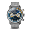 The Shinola Canfield Speedway Open Road Automatic Chronograph Watch features a blue gradient dial with two subdials, orange and blue accents, a tachymeter bezel, Swiss movement, silver mesh band, and elegant silver hands and hour markers.